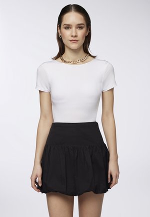 Top bianco aderente con maniche corte, abbinato a una gonna nera a vita alta con volant, caratterizzata da una texture liscia e una vita elasticizzata.