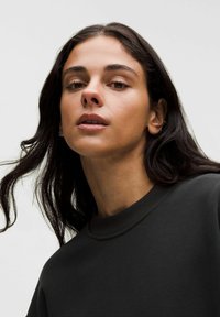 Schwarzer Sweatshirt mit Rundhalsausschnitt und gerippten Bündchen, mit glatter Textur und minimalistischem Design, getragen von einer Person mit langen Haaren.