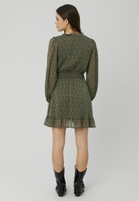 Robe florale verte avec de longues manches transparentes, une taille smockée et un ourlet à volants en couches, assortie à des bottines noires.