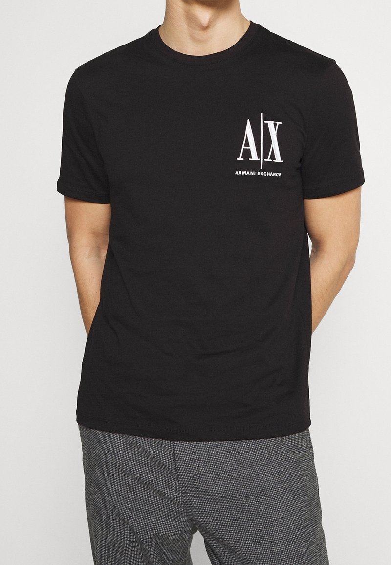 Camiseta de algodón negra con un logo blanco "A|X" y el texto "ARMANI EXCHANGE" en el lado izquierdo del pecho. Cuello redondo, mangas cortas.