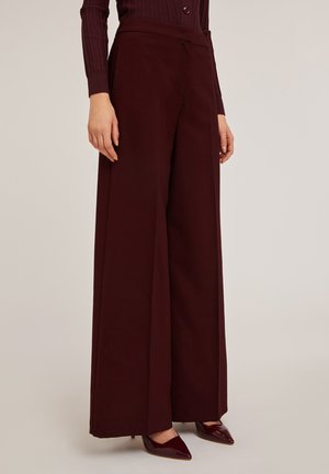 Wide-leg pants in deep burgundy, made from smooth fabric. Features a high waist and seamless finish; paired with pointed burgundy heels.
