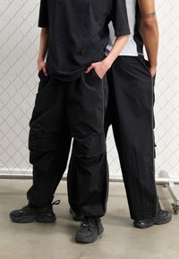 Svarta cargobyxor med en lös passform, texturerat tyg, sidofickor och kontrasterande vita sömmar, ihop med svarta sneakers.