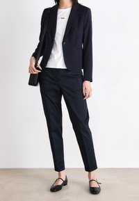 Granatowa marynarka na jedno zapięcie, biała koszulka z logo "BOSS", ciemne spodnie i czarne baleriny. Gładka tkanina, dopasowany krój, minimalistyczny design.