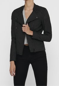 Svart jacka i konstläder med figurnära design, diagonala blixtlås, räfflade axeldetaljer och kort skärning. Texturerad yta.