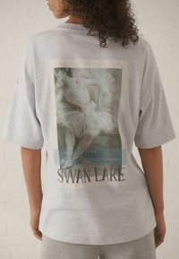 Graues, übergroßes T-Shirt mit einem gedruckten Balletttänzer-Graphic auf der Rückseite, mit dem Text "Schwanensee" und einem Vintage-Veranstaltungsdatum darunter.