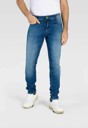 Slim-fit blue denim jeans with a slight fade, featuring a buttoned waistband and five pockets. Paired with white sneakers and a plain t-shirt.