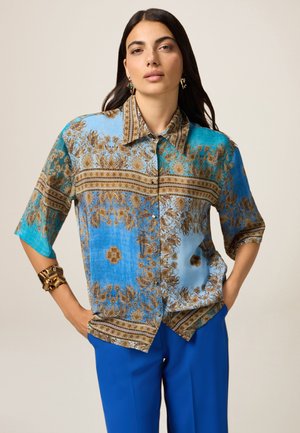 Losse blauwe shirt met sierlijke gouden bloemenpatronen en gestreepte accenten, voorzien van een klassieke kraag en korte mouwen.
