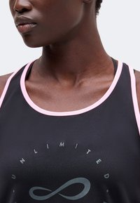 Gros plan d'une personne portant un débardeur noir avec une bordure rose et le mot "UNLIMITED" au-dessus d'un symbole infini.
