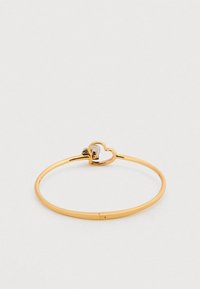 Βραχιόλι με βραχιόλι από μέταλλο σε χρυσή απόχρωση, με άνοιγμα σε σχήμα καρδιάς και λεία, γυαλισμένη επιφάνεια. Απλός σχεδιασμός με ιδιότητες που αντανακλούν το φως.