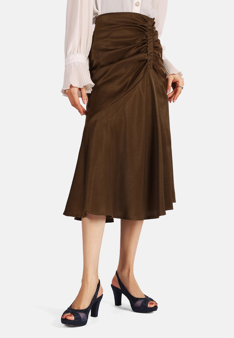 Falda marrón hasta la rodilla con detalle fruncido en la parte delantera, combinada con tacones de color marino con punta abierta que presentan acentos transparentes y un acabado texturizado.