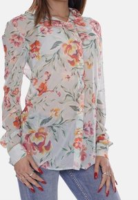 Camicia trasparente con bottoni, decorata con un motivo floreale in colori pastello, caratterizzata da maniche lunghe, colletto e sottili righe verticali.