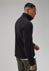 Black fleece jacket with a high collar, featuring a red and blue logo detail at the back neck, slim fit, and soft texture.