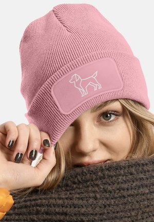 Pink knit beanie featuring a rectangular patch with a white dog silhouette. The fabric is ribbed, and the edge is slightly rolled up.