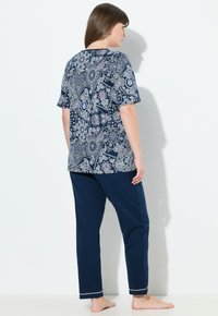 Mörkblå pyjamasset med en kortärmad topp med paisleymönster och enfärgade mörkblå byxor med vit dekorativ söm i fållen.