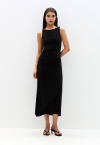 Schwarzes ärmelloses Kleid mit tailliertem Oberteil und Rüschendetails. Verfügt über einen fließenden asymmetrischen Saum und eine glatte, leichte Stofftextur.