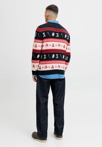 Jersey de punto con un patrón en negro, rojo y crema que presenta motivos festivos; combinado con jeans oscuros y calzado marrón. Textura suave.