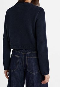 Navy knitted cropped sweater with ribbed hem and cuffs, featuring a textured pattern. Paired with dark blue high-waisted jeans.