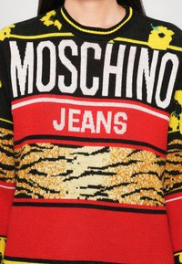 Juodai raudona megztinė su "MOSCHINO JEANS" tekstu, gėlių raštais ir tigro dryžių dizainu geltonos ir smėlio spalvos atspalviuose.