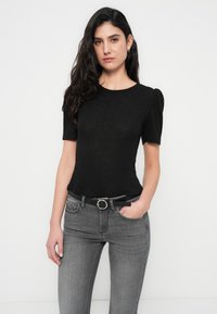 Μαύρο κοντομάνικο τοπ με ριγέ υφή, διακοσμημένο με στρογγυλή λαιμόκοψη και διακριτικά φουσκωτά μανίκια, φορεμένο με γκρι τζιν και μαύρη ζώνη με κυκλικό αγκράφα.