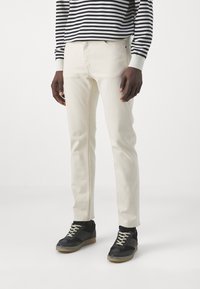 Jeans color beige claro con un corte slim, con una textura suave y costuras mínimas, combinados con zapatillas negras con detalles grises.