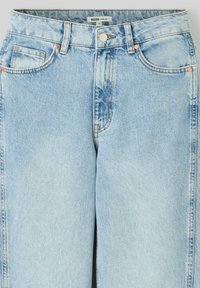 Jeans larges bleu clair en denim, avec des coutures piquées, des poches avant et des accents en métal. Texture lisse, design décontracté.