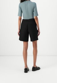 Czarne krótkie spodenki na miarę z bocznymi kieszeniami, wysokim stanem i luźnym krojem. Połączone z jasnoniebieską bluzką z krótkim rękawem.