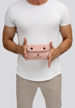 Pochette en silicone rose avec fermeture à rabat, comportant deux boutons-pression noirs et un logo imprimé. Tenue dans les mains devant un fond neutre.