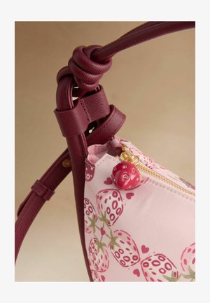 Vaaleanpunainen ja viininpunainen olkalaukku mansikkakuvioilla, solmittu viininpunainen hihna ja vetoketjun vetolaite, joka on punainen leppäkerttu strasseilla.