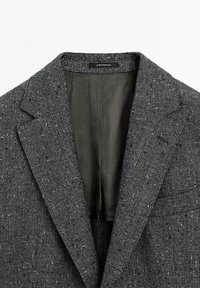 Gray plaid blazer with a textured fabric, wide lapels, and an olive green interior lining. Label reads "Made in Portugal."
