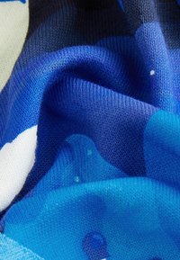 Tessuto blu decorato con un motivo, caratterizzato da una texture liscia, con diverse tonalità di blu e forme bianche, che mostrano un design morbido e lavorato a maglia.