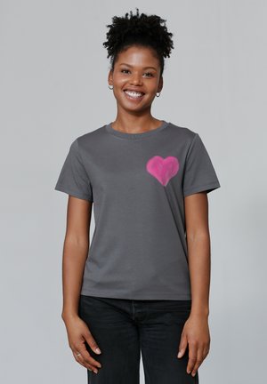 T-shirt en coton gris avec un motif de cœur rose sur la partie gauche de la poitrine. Manches courtes et encolure ronde. Silhouette ajustée.