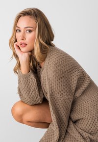 Maglione lavorato a maglia di colore taupe con un motivo testurizzato e maniche ampie, caratterizzato da una vestibilità comoda e dettagli intricati sul tessuto.