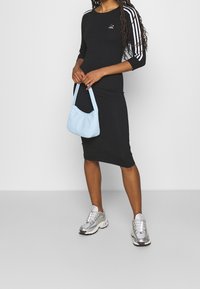 Vestido negro ajustado con tres rayas blancas en las mangas, combinado con un bolso azul claro y zapatillas deportivas plateadas. Textura de tela suave.