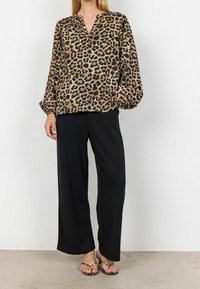 Blouse à imprimé léopard avec col en V, manches longues bouffantes, et pantalon large noir. L'ensemble est complété par des sandales noires et blanches.