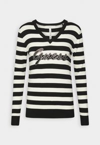 Pull en rayures noir et blanc avec un col en V, accentué par un logo "Guess" en cursive en strass sur la poitrine.