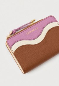 Kompakti lompakko, jossa on vaaleanpunaisia, valkoisia ja ruskeita aaltoilevia nahkapaneeleja, kultainen vetoketju ja kultainen "COCCINELLE"-logo yläpaneelissa.