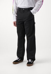 Zwarte cargo-broeken met een relaxte pasvorm, voorzien van zijzakken en een gladde afwerking. Gepaard met zwart-witte sneakers.