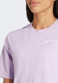 Svetlofialové športové tričko s krátkymi rukávmi, okrúhlym výstrihom a jemnými detailmi šitia. Na hornej ľavej strane má biele logo.