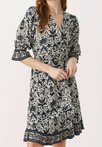 Robe à imprimé floral en crème et bleu marine, dotée d'un design croisé, de manches bouffantes et d'un ourlet évasé avec des détails de bordure complexes.