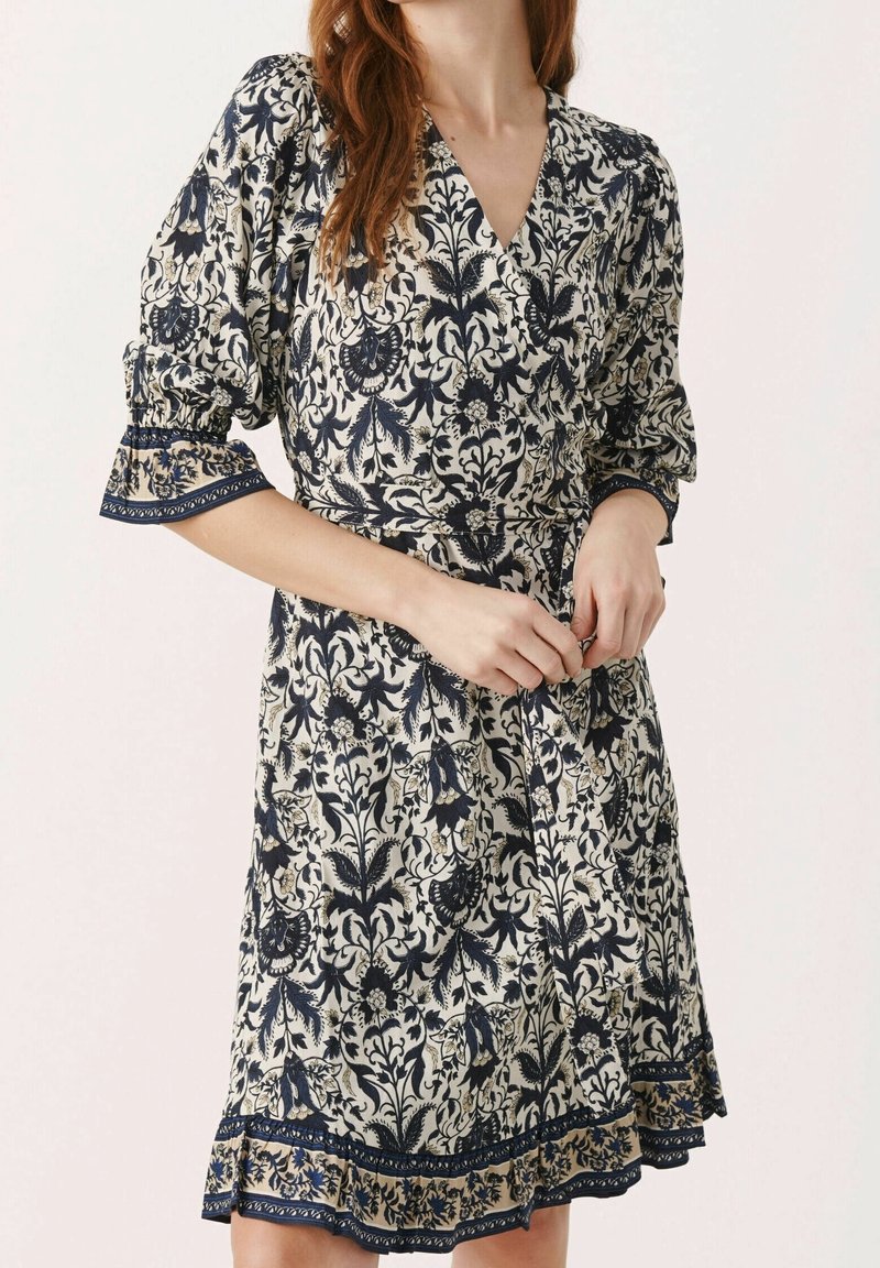 Robe à imprimé floral en crème et bleu marine, dotée d'un design croisé, de manches bouffantes et d'un ourlet évasé avec des détails de bordure complexes.