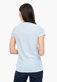 Vaaleansininen lyhythihainen T-paita, jossa on pyöreä pääntie, hienovarainen tekstuuri, rento mitoitus ja suora helma. Yhdistetty tummiin farkkuihin.