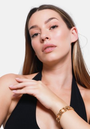 Gouden kettingarmband om de pols, gladde metalen schakels, contrasterend met zwarte stoffen top, hand delicieus nabij de schouder geplaatst.