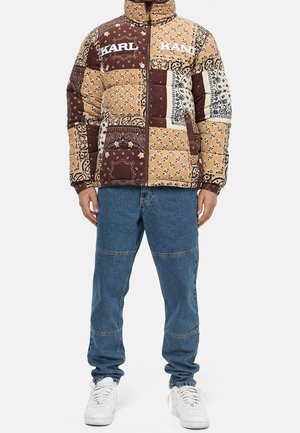 Gewatteerd jack in patchwork ontwerp met bruine, beige en witte kleuren. Geaccentueerd met bloemmotieven en merklogo's. Draagt blauwe spijkerbroek.