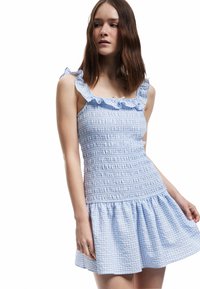 Blauwe en witte geruite jurk met schouderbanden met ruches, een smocked lijfje en een flared rok, gemaakt van lichtgewicht stof.