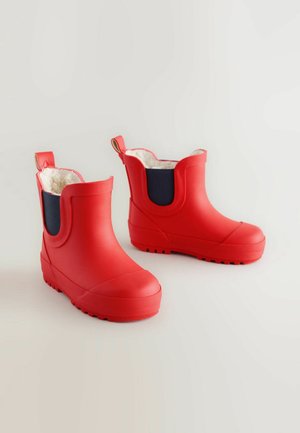 Bottes en caoutchouc imperméables rouges avec une texture lisse, un design à la cheville basse et des panneaux latéraux en bleu marine. Elles disposent d'une doublure en fourrure douce et de languettes à l'arrière.