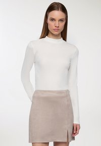 Top bianco a maniche lunghe con colletto alto, abbinato a una gonna corta in suede marrone chiaro con uno spacco frontale. Tessuto liscio uniforme in tutto.