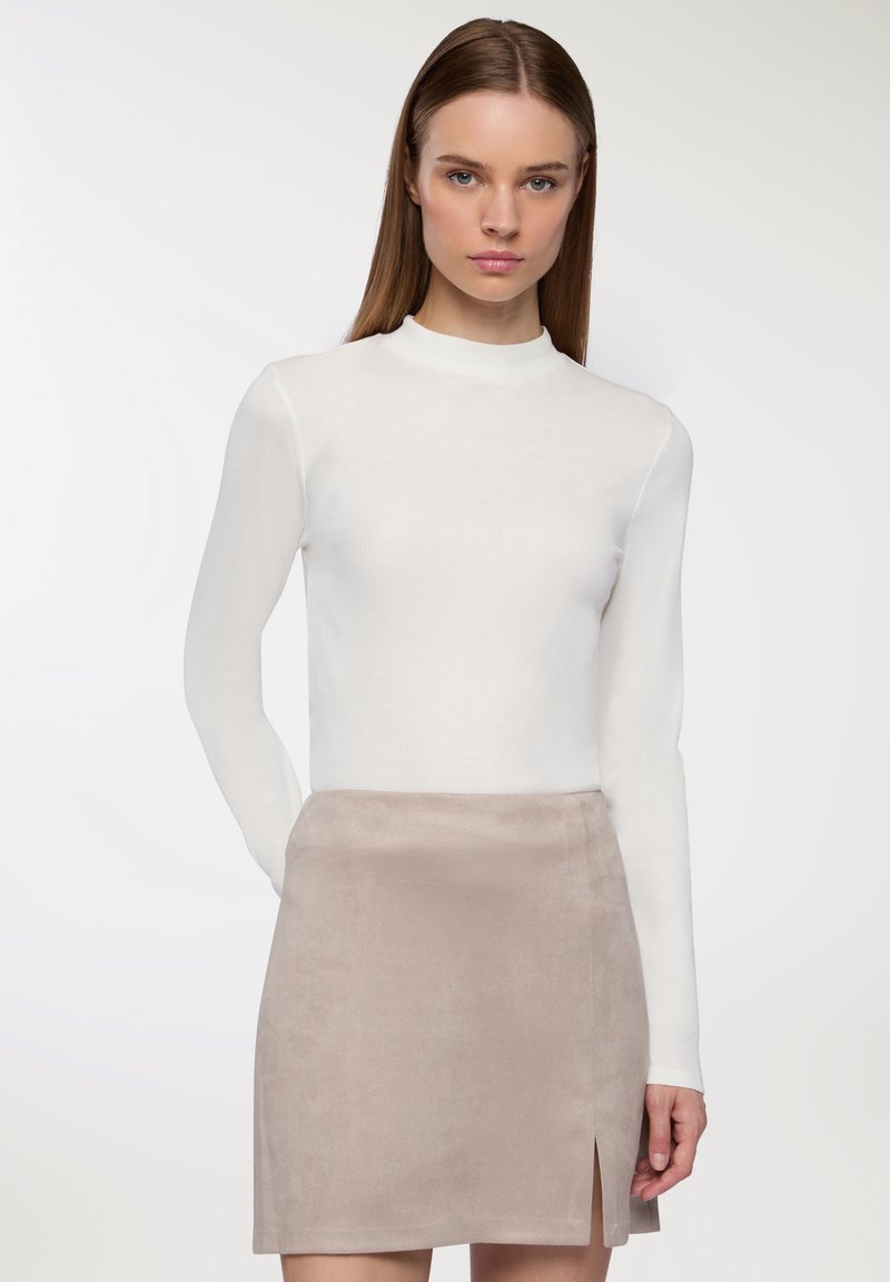 Top bianco a maniche lunghe con colletto alto, abbinato a una gonna corta in suede marrone chiaro con uno spacco frontale. Tessuto liscio uniforme in tutto.