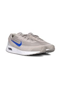 Grijze sportschoenen met een bovenwerk van mesh en suède, met een blauwe Nike swoosh, een witte tussenzool en een gestructureerde rubberen buitenzool.