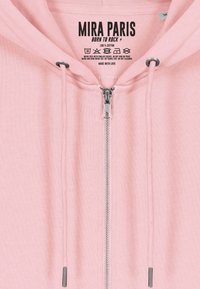 Felpa zip con cappuccio di colore rosa chiaro realizzata in 100% cotone. Presenta una zip YKK e lacci con dettagli metallici. Istruzioni per la cura stampate all'interno.