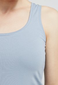 Light blue sleeveless tank top made of soft, stretchy fabric. It features a rounded neckline and smooth, even stitching.